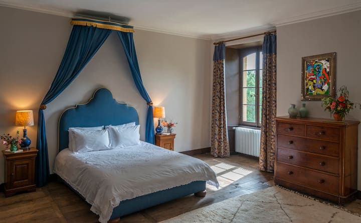 Bedroom #1, double bed, adorned with a  blue headboard and crisp linens, offers a peaceful haven for a restorative sleep within the château's historic walls.