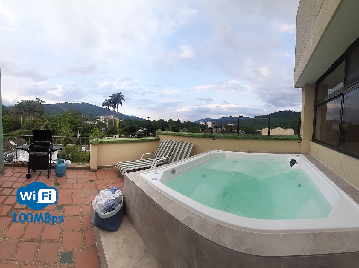 A private terrace features a spacious jacuzzi surrounded by scenic views of greenery and hills. A gas BBQ grill is positioned nearby, along with lounge chairs. The area is designed for relaxation and enjoyment, with WiFi access indicated nearby.