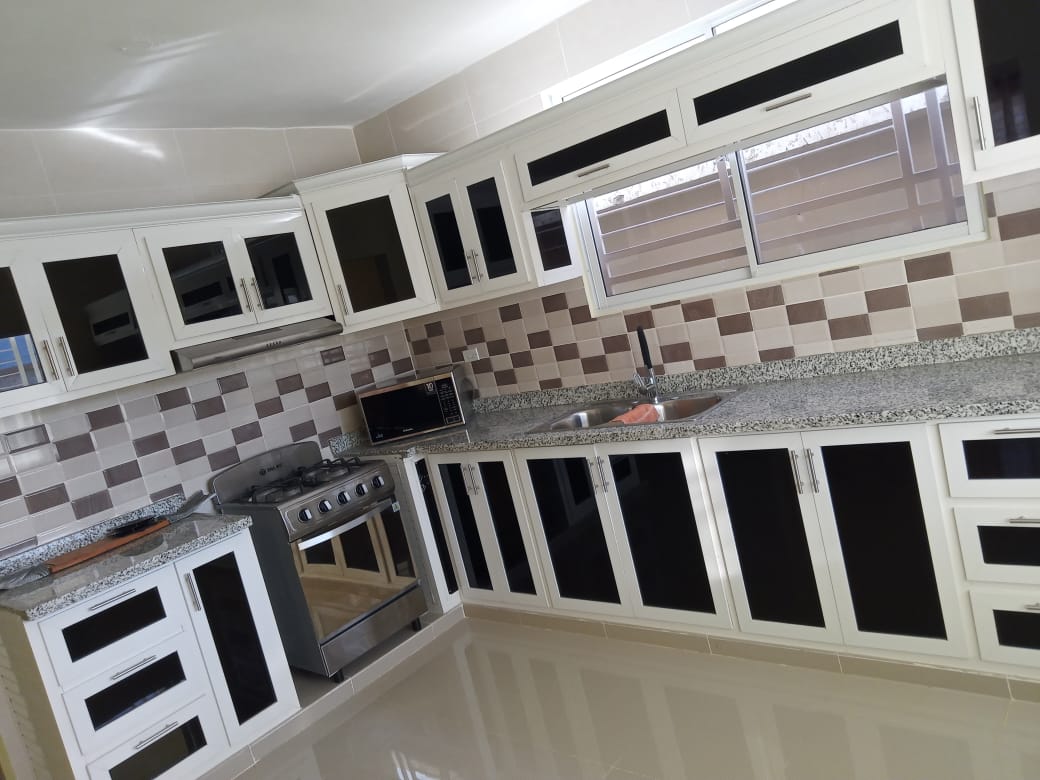 A modern kitchen is presented with sleek white cabinetry featuring black glass accents. The countertops are covered in a light grey granite, while a stainless steel stove and microwave are strategically placed. Large windows allow natural light to fill the space, enhancing its functionality.