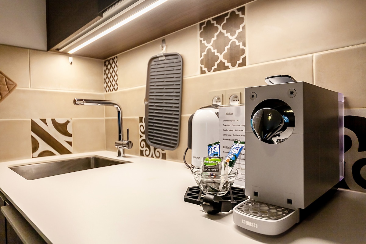 A modern kitchen countertop features a sleek Nespresso coffee machine beside a glass holding various coffee capsules. Decorative tiles add character to the backsplash, while a convenient sink is located on the left. A functional design is evident throughout the space.