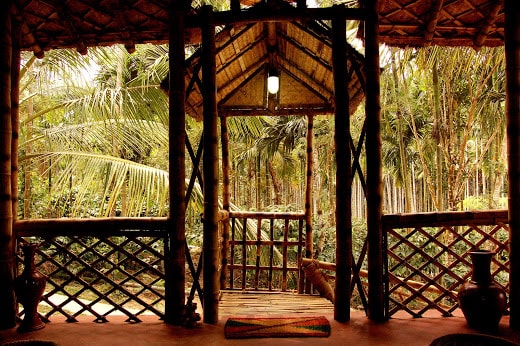 An airy entrance features a wooden framework with bamboo accents, allowing natural light to fill the space. A view of lush greenery is visible through the open doorway, enhancing the connection with the surrounding nature.