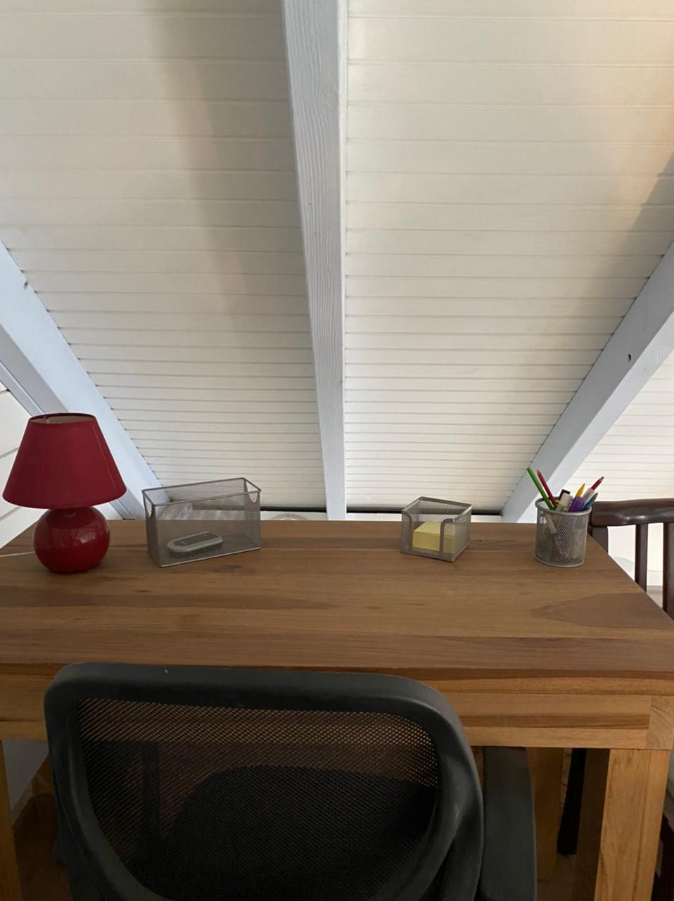 An organized workspace features a wooden desk equipped with a mesh office chair. A small red lamp provides lighting, while two glass containers hold office supplies. A cup filled with assorted pens sits to the right, enhancing the functional design of the area.