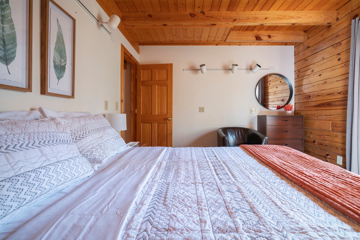 ห้องนอนชั้นแรกออกจากห้องครัวและตรงข้ามกับห้องอาบน้ำเต็มรูปแบบชั้นหลัก เตียงควีนไซส์พร้อมหน้าต่างเมื่อมองออกไปในป่า 