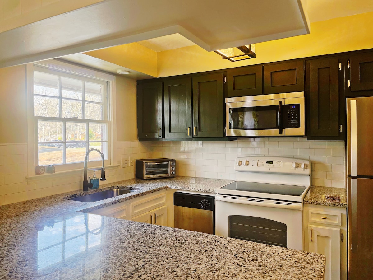 A well-appointed kitchen features dark cabinetry and stainless steel appliances, including a microwave and a refrigerator. A granite countertop provides ample workspace, while a window allows natural light to illuminate the area, creating a bright and functional cooking environment.
