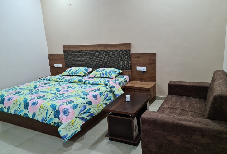A well-furnished sleeping area is presented, featuring a spacious bed adorned with a floral patterned cover. A nearby coffee table and a comfortable sofa provide additional seating. Soft lighting enhances the inviting atmosphere against a neutral wall backdrop.