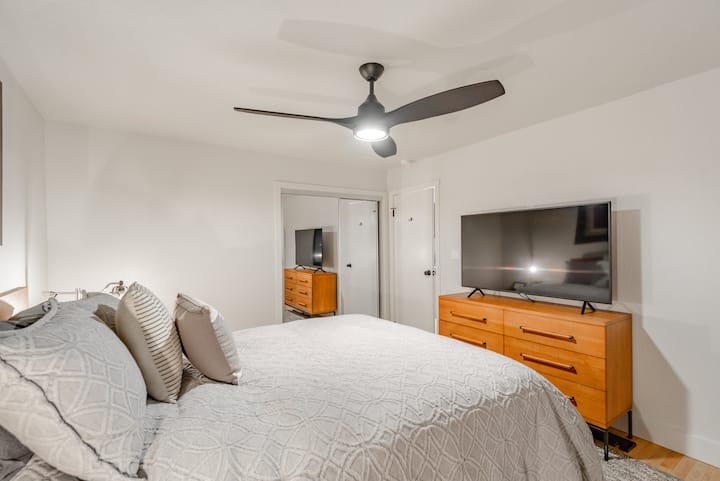 Dhomë gjumi në katin e poshtëm me krevat dopio "queen", komodinë, ventilator tavani dhe televizor 55'.