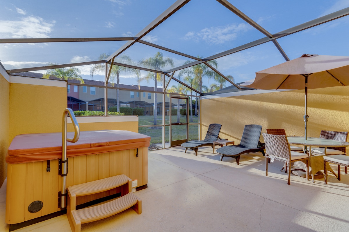 A screened private patio features a relaxing Jacuzzi alongside outdoor loungers and a dining table. Bright sunlight casts shadows on the patio floor, while palm trees line the background, adding a tropical feel to the space.