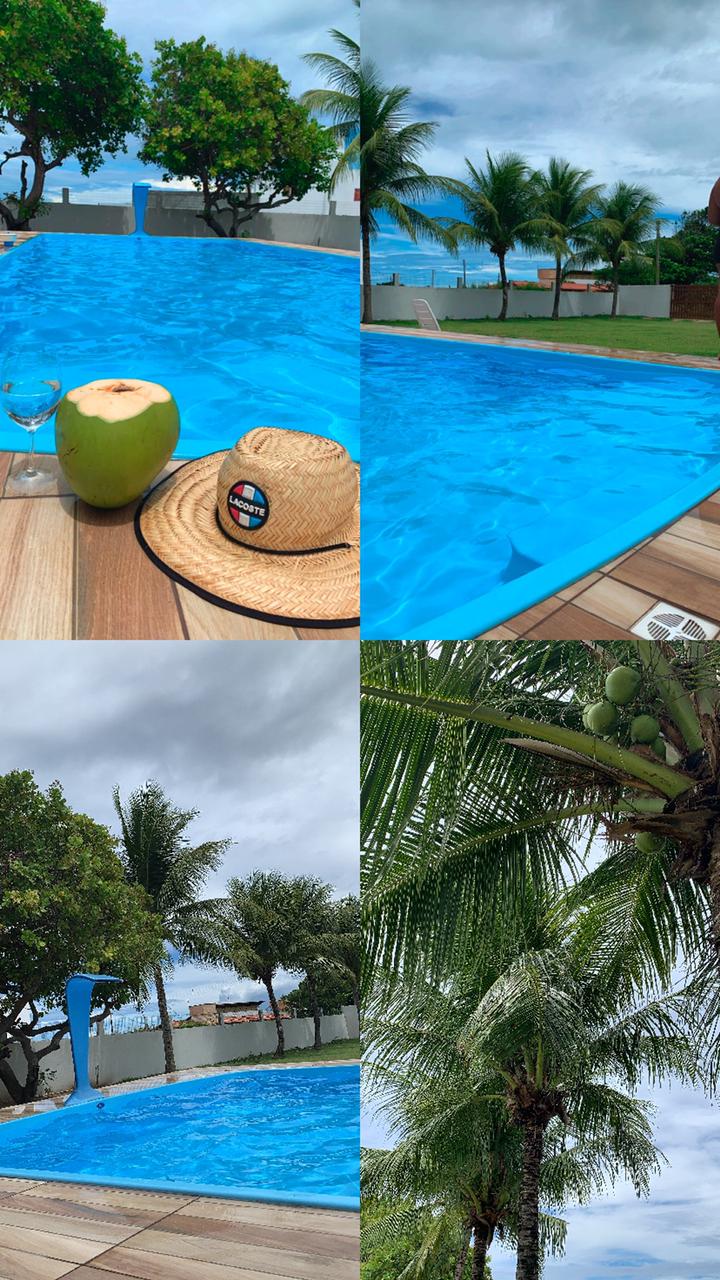 A spacious pool with crystal clear water is surrounded by wooden decking, showcasing vibrant greenery. Coconut trees frame the area, adding a tropical touch. The scene is complemented by a straw hat and a glass of coconut water resting on the edge of the pool.