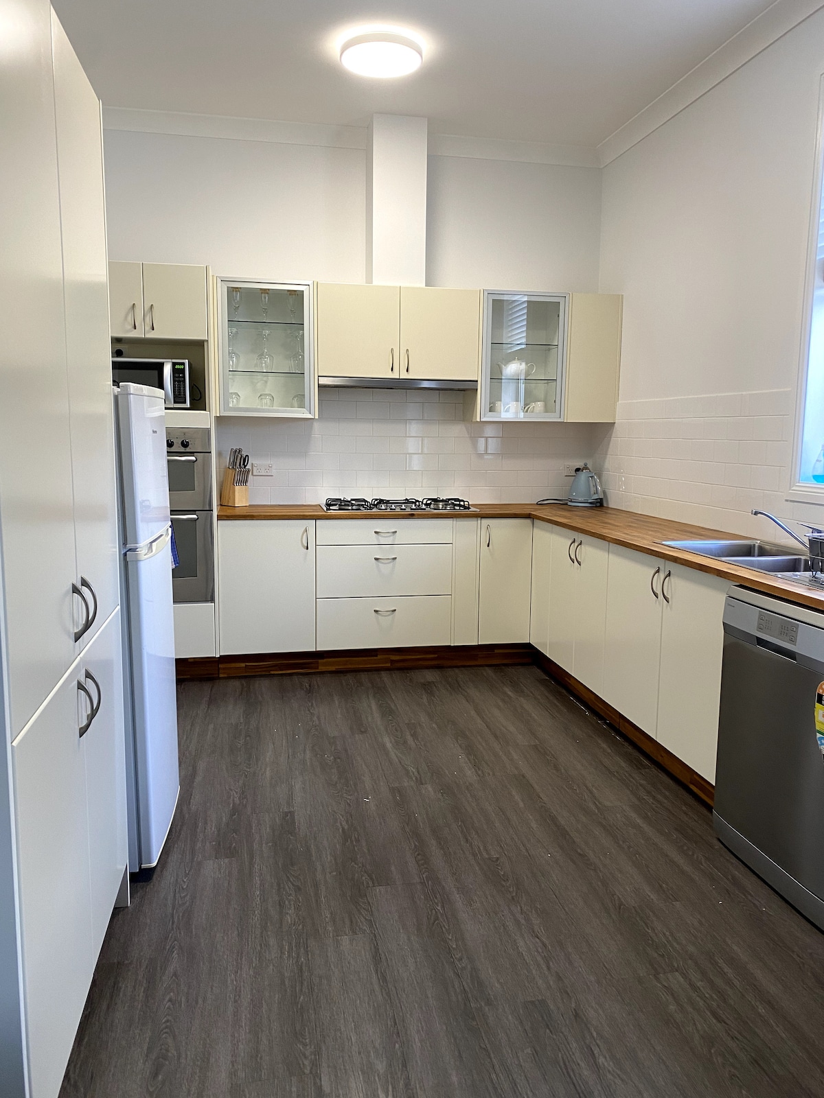 The kitchen features modern cabinetry with a clean design and a spacious countertop. Appliances include a refrigerator, oven, and dishwasher. Natural light enters through a window above the sink, creating a functional and well-lit cooking space.