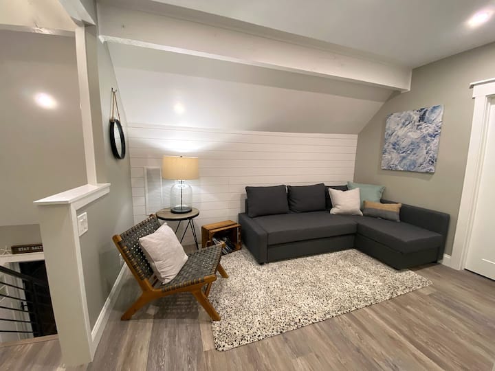 En montant les escaliers, vous trouverez la suite principale. Il s'agit du salon, avec canapé sectionnel (qui se transforme en lit) et chaise d'appoint.