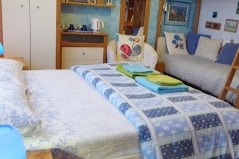 A comfortable sleeping area is presented with a spacious bed layered with a patterned blanket and neatly arranged towels in blue and green hues. A small seating area features a cozy chair and a side table, complemented by a decorative arrangement on the walls.