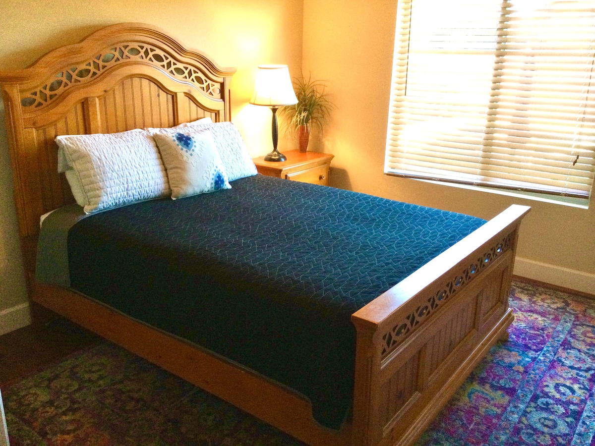 Dormitorio en la planta baja con cama tamaño queen, mesita de noche, cómoda y vistas a la piscina del patio trasero. 