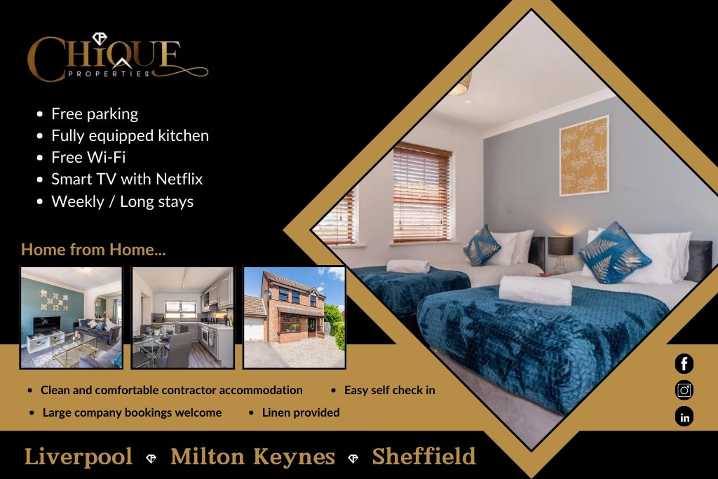 The image displays a well-lit room featuring twin beds with blue bedspreads and decorative cushions. Natural light filters through the window with wooden blinds. Soft grey walls complement the modern decor, including framed artwork above the beds, creating a serene atmosphere.