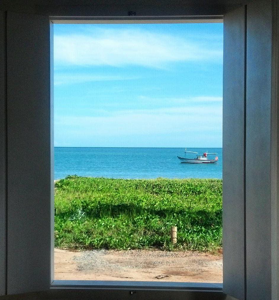 A serene view is framed by a large window, showcasing a boat gently floating on calm waters. The surrounding landscape features lush greenery and the horizon meeting the clear blue sky.