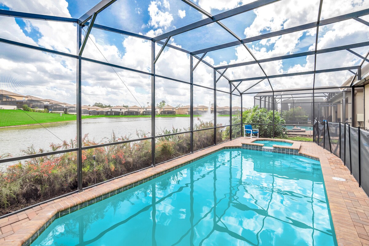 A private pool area is enclosed by a screen, showcasing a clear blue pool bordered by a brick deck. Lush greenery surrounds the space, offering a scenic view of the serene lake in the background, complementing the tranquil atmosphere.