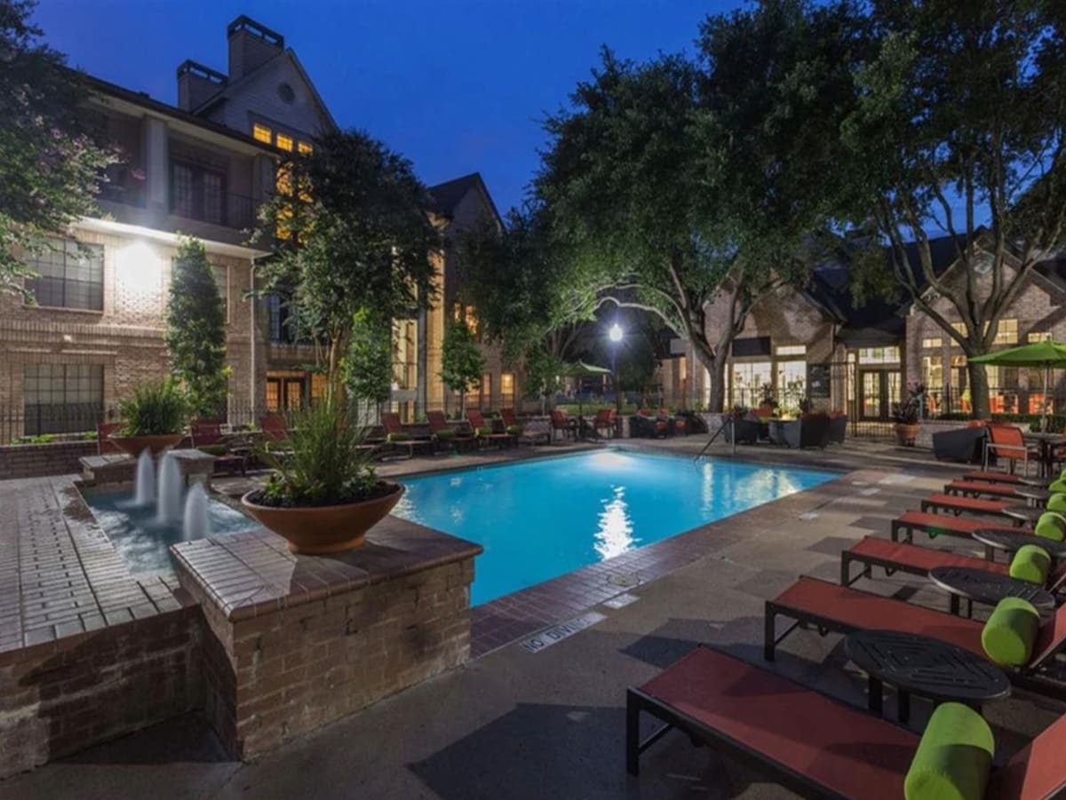 A resort-style pool is surrounded by lush landscaping and comfortable lounge chairs. Soft lighting highlights the outdoor seating areas and the tranquil water features, creating a relaxing environment for guests to unwind.