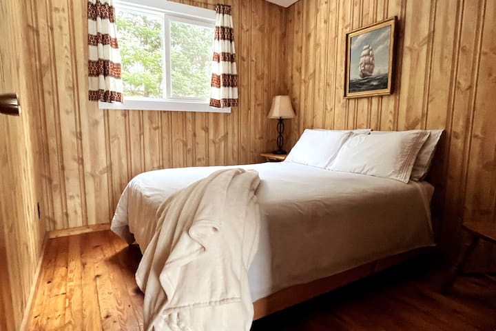 Bedroom 2 with double bed, crisp, clean linens, extra pillows, cozy blanket & east-facing window to capture the morning sunshine.  Shelves out of view to the right for storage.