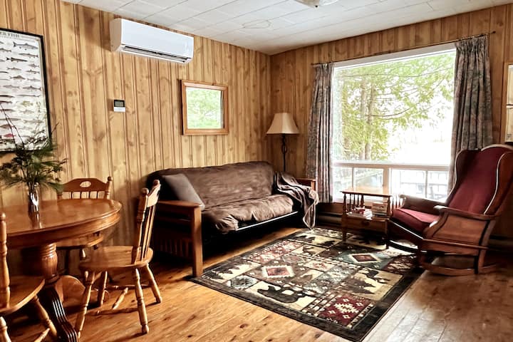 Dining/living area with futon (sleeps 2) and comfy rocker.  Seating for 6 at the dining table with leaf and extra chairs from the bedrooms.  Large picture window brightens your day and overlooks the deck, yard, lake & stunning sunsets!