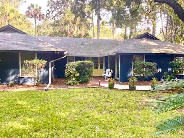 The exterior of a ranch-style home surrounded by lush greenery and tall trees. A grassy area leads to a welcoming entrance, featuring a pathway and potted plants. Seating areas are visible near the entrance, enhancing the inviting outdoor space.