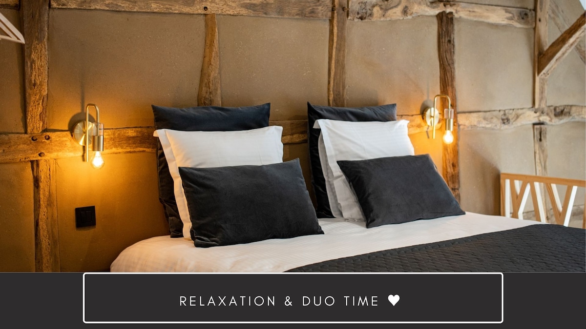 A spacious sleeping area features a comfortable bed with two sets of pillows and soft bedding. Warm lighting is provided by stylish wall sconces on either side, creating an inviting space for relaxation.