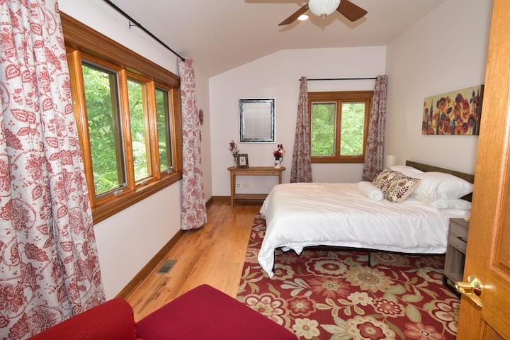 Spavaća soba s crvenim cvijećem na katu ima bračni krevet i stolicu za opuštanje i uživanje u jutarnjoj kavi i pogledu.