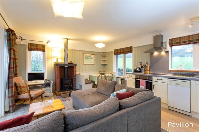 An open-plan living space showcases a comfortable gray sofa, inviting natural light through large windows. A wood-burning stove provides warmth, while a dining area is adjacent to a well-equipped kitchen. Subtle tones and textures create a relaxing environment, complemented by scenic views of the outdoors.