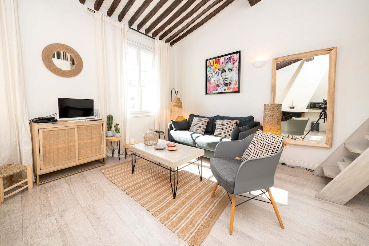 A bright living area showcases a comfortable sofa adorned with patterned cushions and a coffee table positioned on a soft area rug. Natural light filters through a window, and a large mirror reflects the space. A flat-screen TV and decorative items enhance the inviting atmosphere.