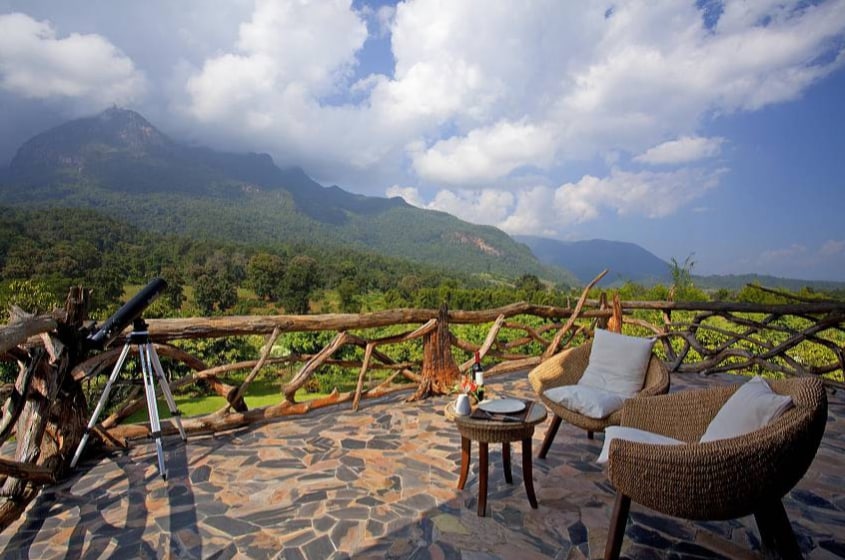 An outdoor terrace offers scenic mountain views, with a telescope positioned beside a small table and a comfortable chair. The rustic railing complements the natural surroundings, and the stone flooring features an earthy palette, enhancing the serene atmosphere of the retreat.