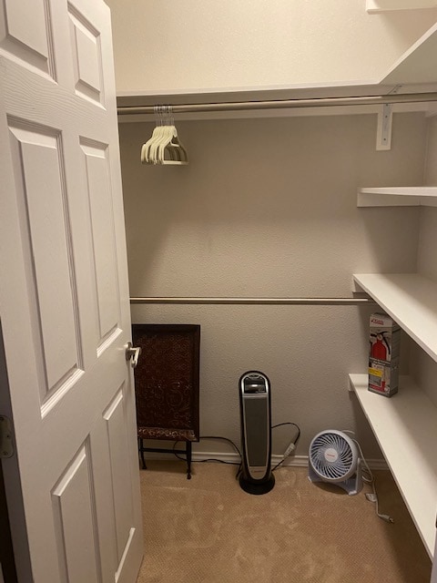A spacious closet features several shelves and a clothing rod for hanging garments. A small fan and a compact heater are positioned on the floor, alongside a decorative folding chair. The interior is well-lit, with a calming beige carpet covering the floor.