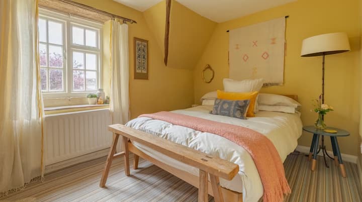 De zonnige, gele slaapkamer kijkt direct uit op de tuin van het huisje en is de perfecte plek om de vogels in de tuin te horen tjilpen. Deze gezellige slaapkamer heeft een tweepersoonsbed en ligt pal naast de familiebadkamer.