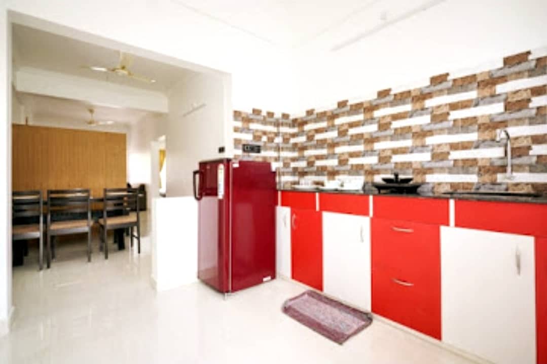 The kitchen area features a modern design with a combination of red and white cabinetry. A red refrigerator is positioned next to the counter, with a textured backsplash of neutral tones. A dining area with wooden chairs is visible in the background.