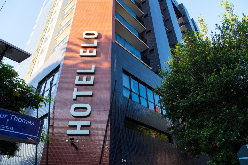 The exterior of Hotel Elo is captured from a low angle, showcasing its modern architecture and large windows. The name 'HOTEL ELO' is prominently displayed in bold letters on the building's facade, framed by the greenery of surrounding trees.