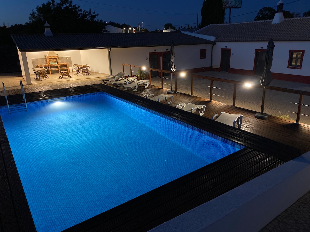 An illuminated salt-water pool is showcased at night, surrounded by comfortable loungers and the inviting glow of outdoor lighting. A spacious terrace with dining furniture is visible in the background, enhancing the outdoor leisure space.