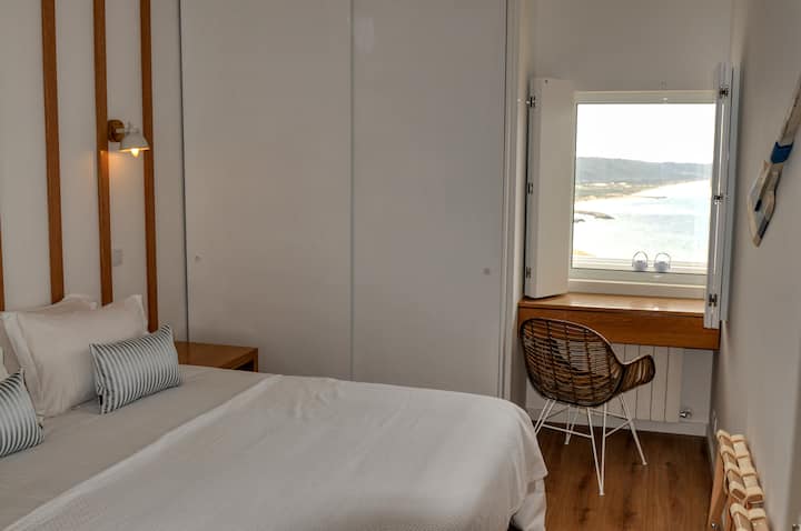 The main bedroom — king-size bed (180 × 200 cm), corner ocean view window, blackout wooden shutters, large quiet ceiling fan, dimmable wall lighting, and a dedicated work desk with a truly inspiring view.