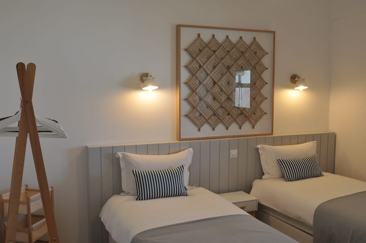 The second bedroom — two single beds (90 × 200 cm) that combine into a king-size bed (180 × 200 cm), blackout wooden shutters, large quiet ceiling fan, and dimmable wall lighting. Set up based on your booking size or request.