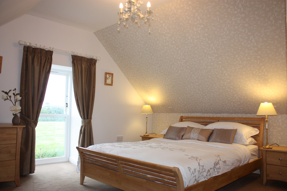 חדר שינה קינג סייז עם מקלחת צמודה מעל אמבטיית ספא. זה בקומה הראשונה ומשקיף על מרעה.