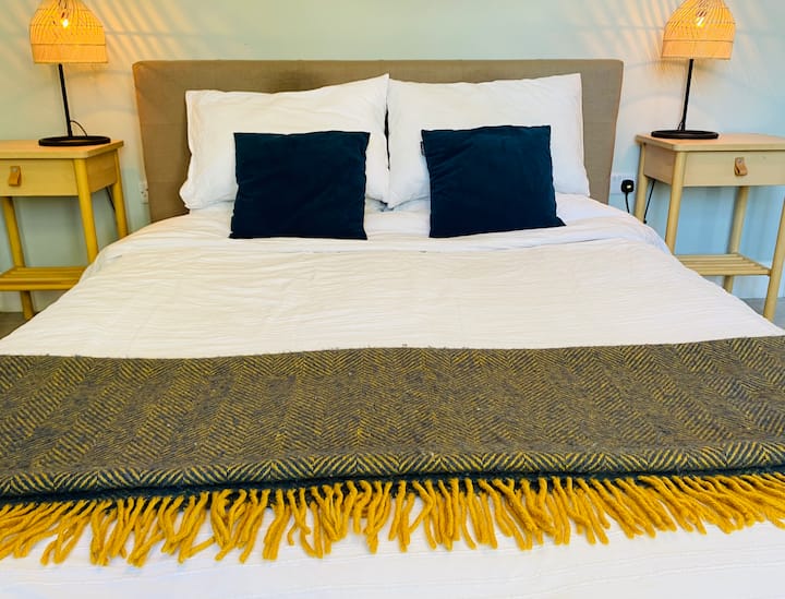 חדר שינה גדול, מואר ומאוורר עם מיטת קינג סייז ונופים המשקיפים על גנים בוגרים.