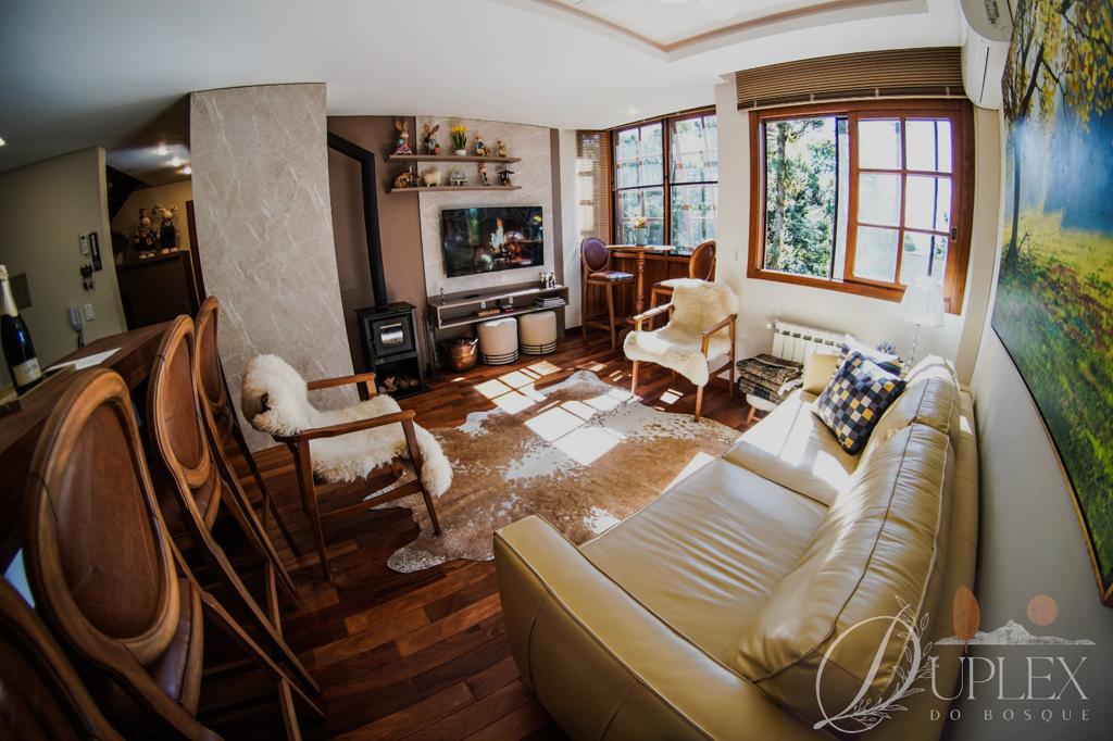 A well-lit living area features large windows providing ample natural light. Comfortable seating options include a beige couch and stylish armchairs. A fireplace is positioned on a stone feature wall, while a dining bar is visible in the background, enhancing the space’s inviting atmosphere.