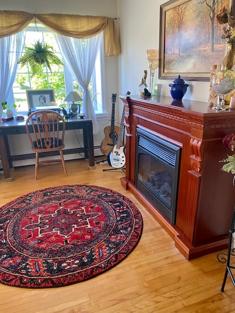 A cozy living space is highlighted by a decorative area rug with intricate patterns. A wooden desk is positioned near a window, accompanied by a wooden chair. A guitar rests beside a fireplace, adding to the inviting atmosphere.