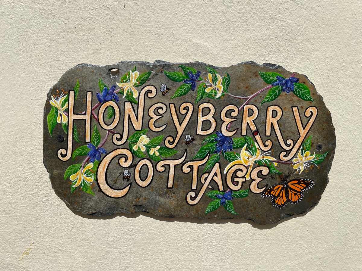 A decorative sign featuring the name 'Honeyberry Cottage' is mounted on the wall. The sign is crafted from stone with colorful painted flowers and a butterfly, which enhance its rustic charm.