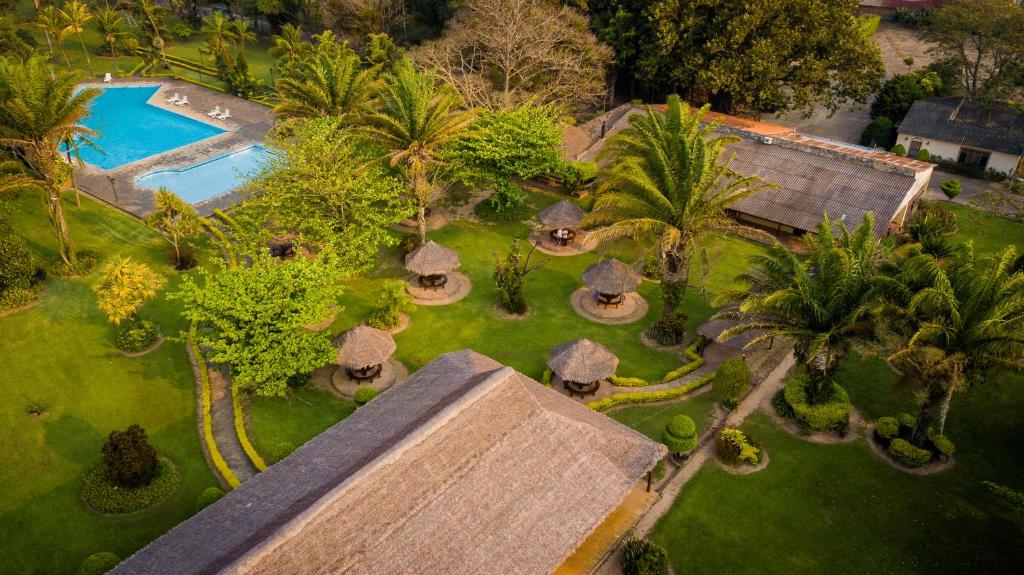 An aerial view captures the lush green landscape surrounding a large swimming pool. Thatched-roof gazebos are nestled among the palm trees and manicured gardens, inviting relaxation in a serene environment.