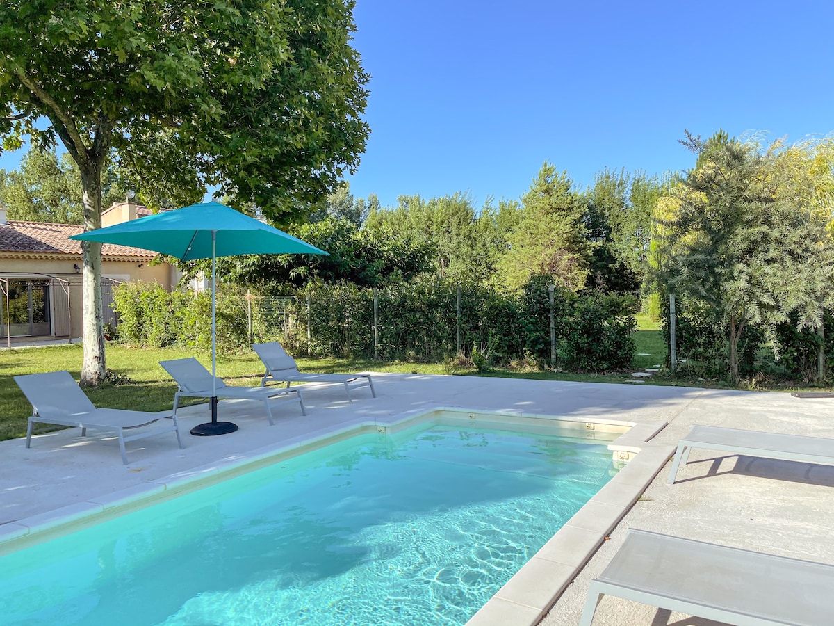 A serene outdoor area features a non-heated swimming pool surrounded by a spacious deck. Sun loungers are positioned near the pool, and a large umbrella provides shade. Lush greenery creates a tranquil backdrop, enhancing the peaceful outdoor setting.