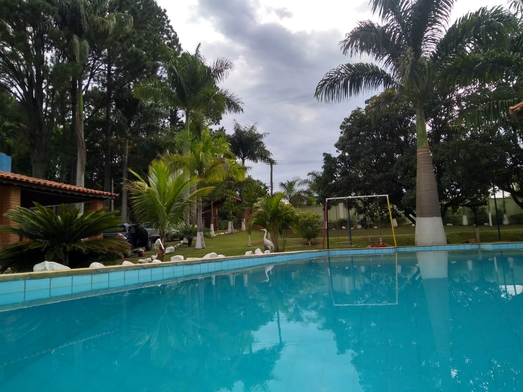 A clear swimming pool is framed by lush greenery, featuring tall palm trees and manicured lawns. The area is enhanced by a swing set visible in the background, contributing to a family-friendly environment.