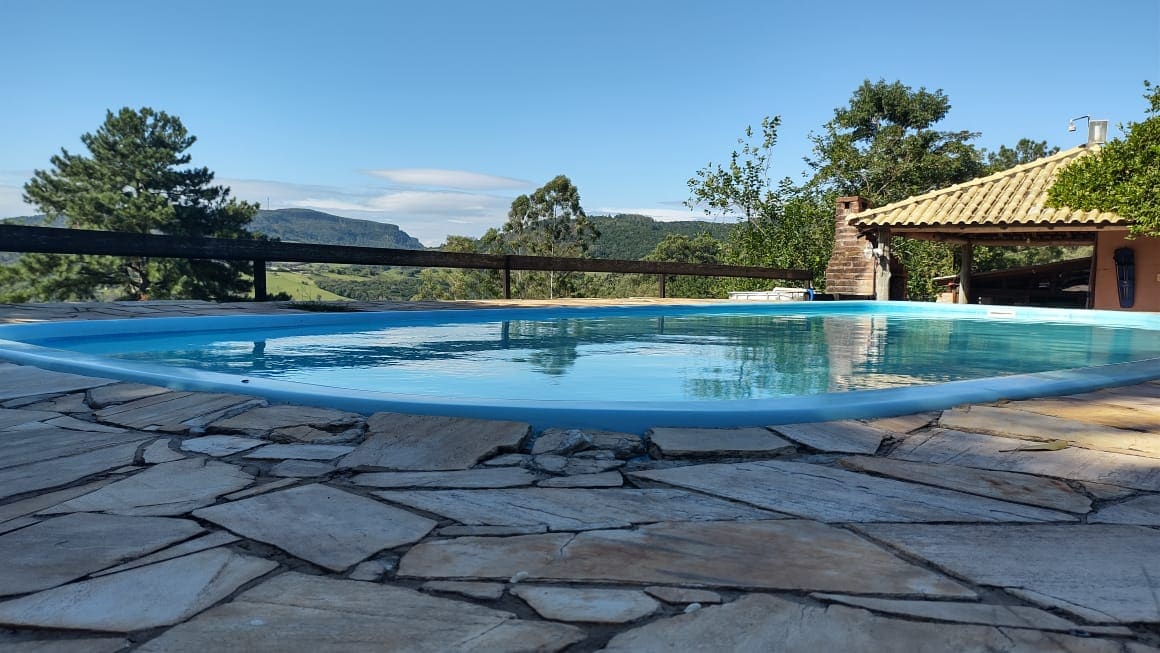 A serene swimming pool with a gently curved edge is set on a stone patio. Surrounding greenery and distant hills can be seen in the background, creating a peaceful and natural atmosphere.