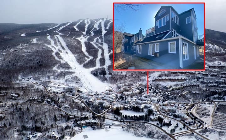An aerial view captures the serene Mont Tremblant landscape, featuring snow-covered slopes and a cluster of buildings. The highlighted condo stands out, showcasing its distinctive architecture amidst a backdrop of winter scenery.