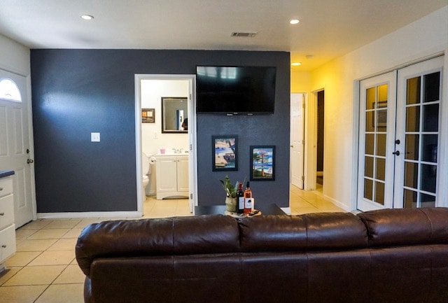 A living area features a chocolate-brown sofa positioned against a dark accent wall. A mounted television is visible above a console table, while framed artwork adorns the wall. Doorways lead to a bathroom and bedrooms, with French doors offering separation from the adjacent space.