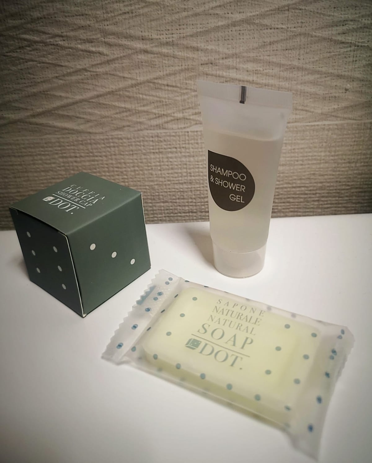 A small box of natural soap sits beside a clear tube of shampoo and shower gel. The soap is wrapped in a polka-dot design, while the shampoo tube features a minimalistic label that indicates its dual purpose.