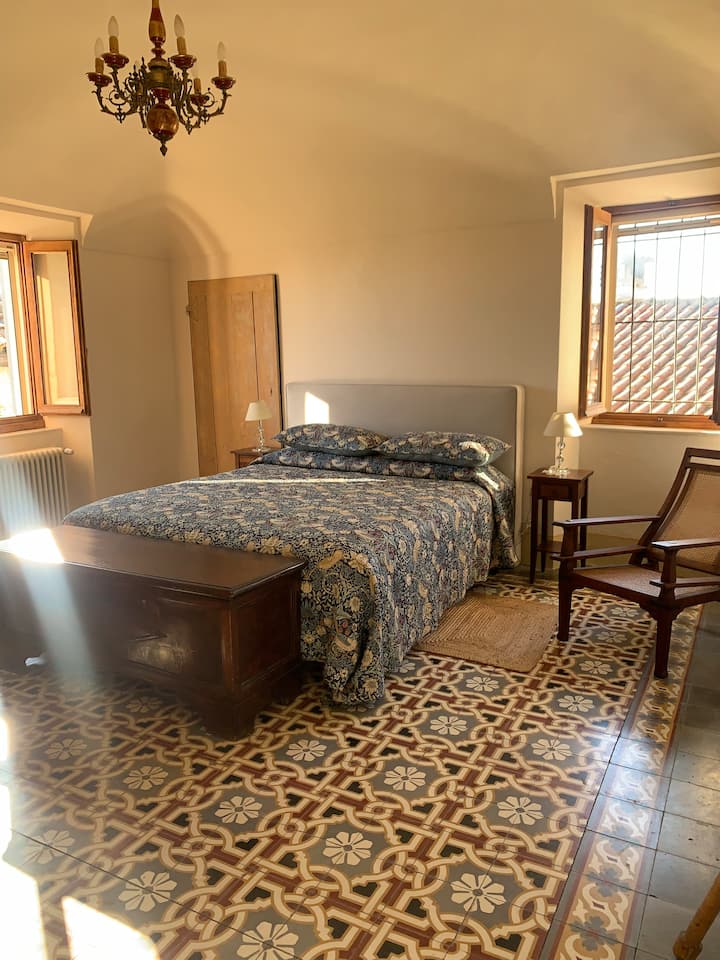 Dhomë gjumi kryesore me krevat dopio "king size" dhe oxhak. Plot dritë me pamje nga kodrat.