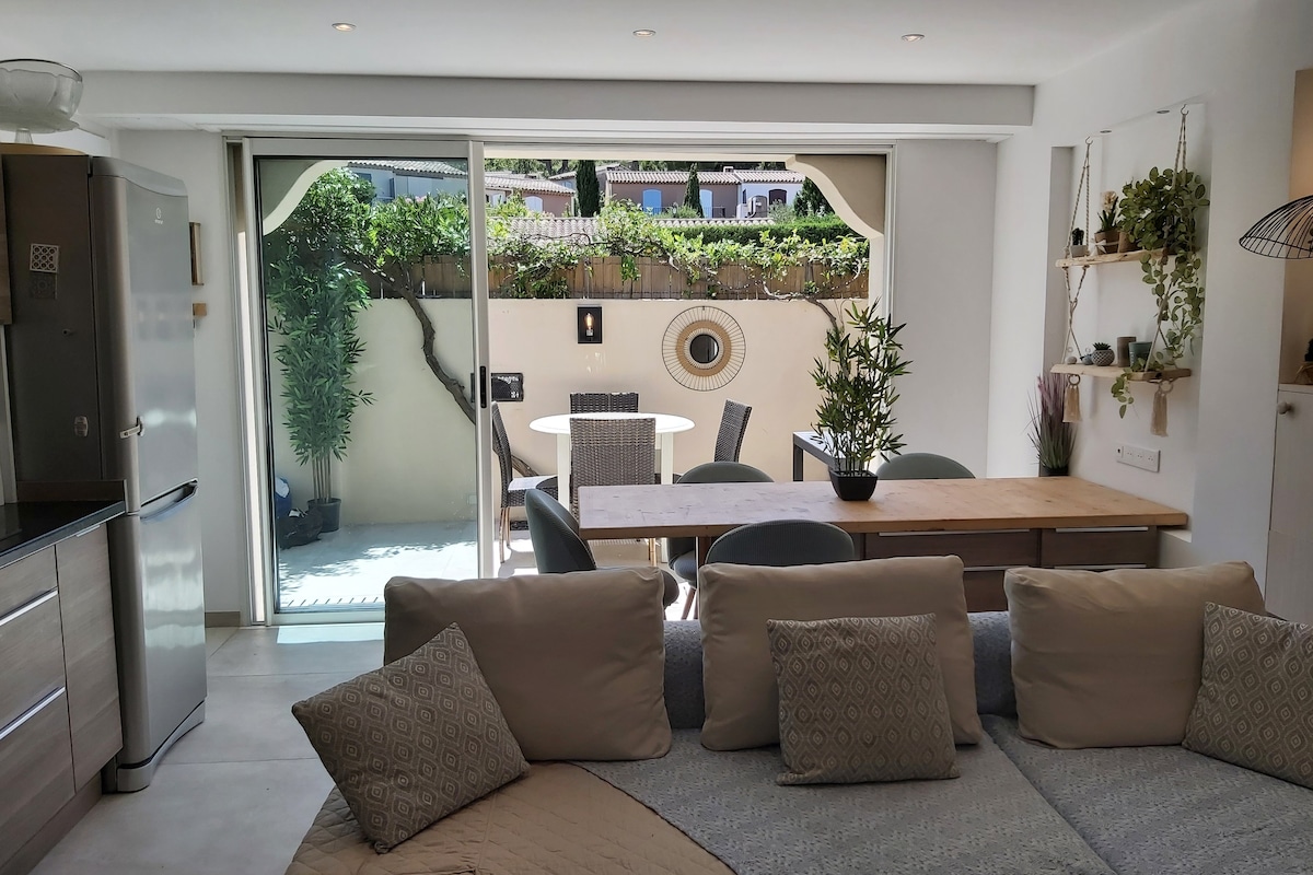 The open-plan living area features a comfortable seating arrangement and a dining table with chairs. A sliding glass door allows natural light to fill the space and offers views of a private terrace adorned with potted plants.
