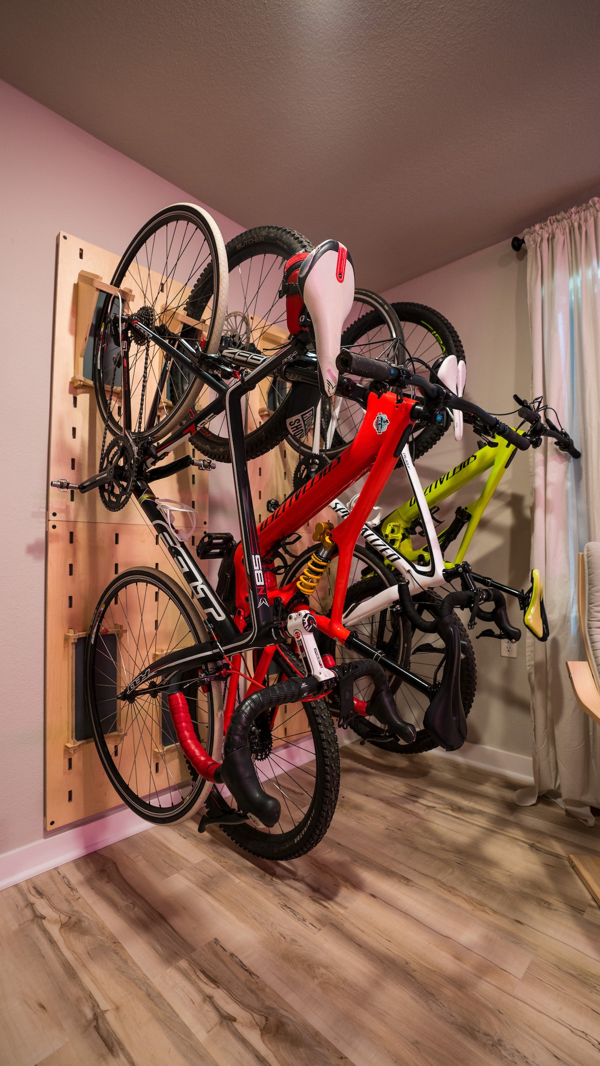 A functional bike storage wall is displayed, showcasing three bicycles securely mounted. The bikes feature varied colors, including red, yellow, and black. The wall's natural wood design complements the modern interior, and a light-colored floor contrasts with the vibrant bicycles.